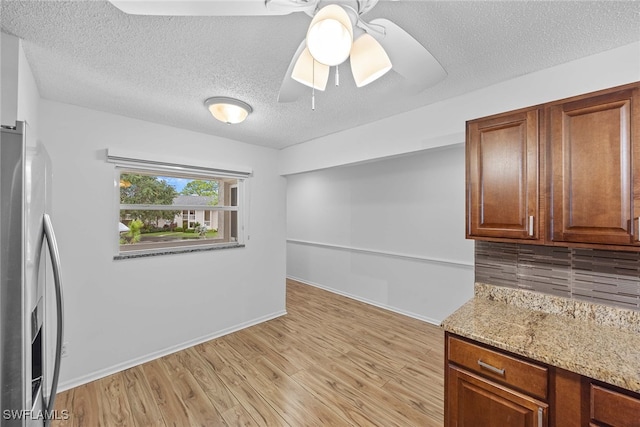 kitchen with light wood-type flooring, light stone counters, a textured ceiling, stainless steel refrigerator with ice dispenser, and ceiling fan