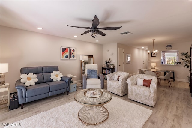 living room with ceiling fan with notable chandelier and light hardwood / wood-style flooring