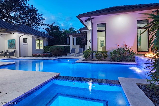 pool at dusk with pool water feature and a patio