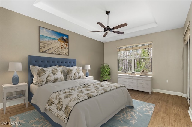 bedroom with a raised ceiling, ceiling fan, and light hardwood / wood-style flooring