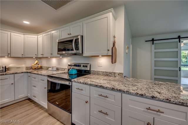 kitchen featuring light stone counters, light hardwood / wood-style floors, white cabinetry, a barn door, and stainless steel appliances