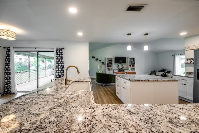 kitchen featuring light wood-type flooring, hanging light fixtures, a kitchen island with sink, and sink