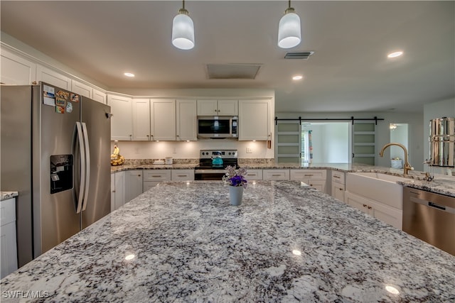 kitchen featuring a barn door, hanging light fixtures, stainless steel appliances, and white cabinets