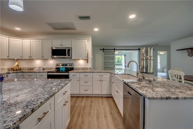 kitchen featuring white cabinetry, a barn door, stainless steel appliances, light wood-type flooring, and sink