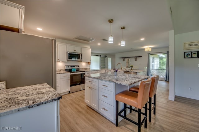 kitchen with appliances with stainless steel finishes, hanging light fixtures, white cabinetry, a kitchen island, and light hardwood / wood-style flooring