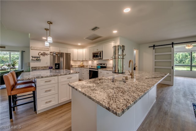 kitchen with a barn door, hanging light fixtures, stainless steel appliances, and a spacious island