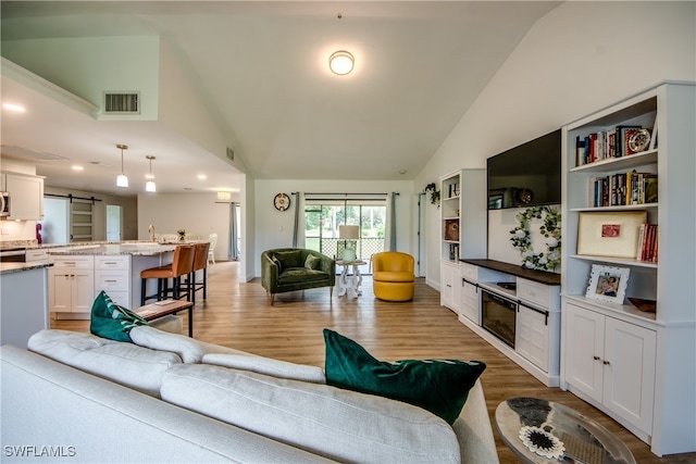 living room featuring a barn door, light wood-type flooring, and high vaulted ceiling