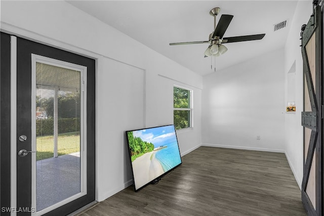 unfurnished room with a barn door, ceiling fan, and dark wood-type flooring