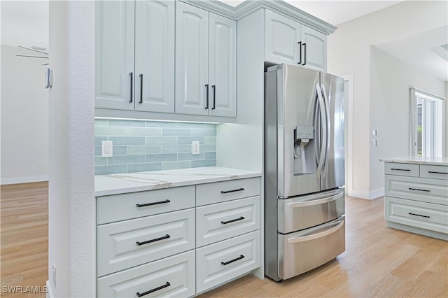 kitchen featuring light stone counters, stainless steel refrigerator with ice dispenser, light hardwood / wood-style flooring, and decorative backsplash