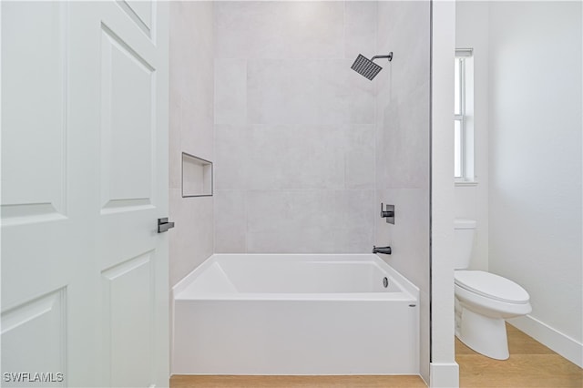 bathroom with hardwood / wood-style flooring, tiled shower / bath combo, and toilet