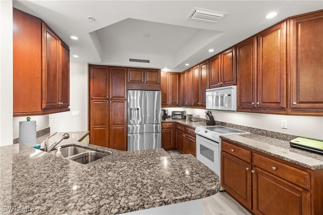 kitchen with dark stone countertops, white appliances, sink, and a tray ceiling