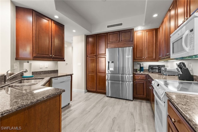 kitchen featuring sink, dark stone counters, white appliances, and light hardwood / wood-style flooring