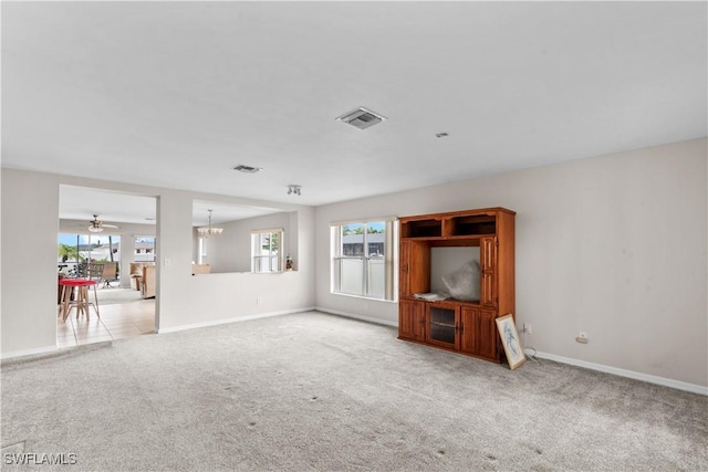 unfurnished living room featuring ceiling fan with notable chandelier, a wealth of natural light, and light colored carpet