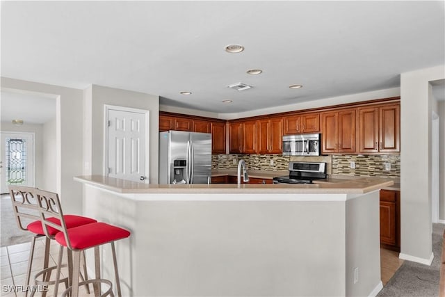 kitchen featuring stainless steel appliances, a breakfast bar, light tile patterned floors, and backsplash