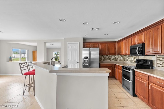 kitchen featuring light tile patterned floors, a breakfast bar area, backsplash, stainless steel appliances, and an island with sink