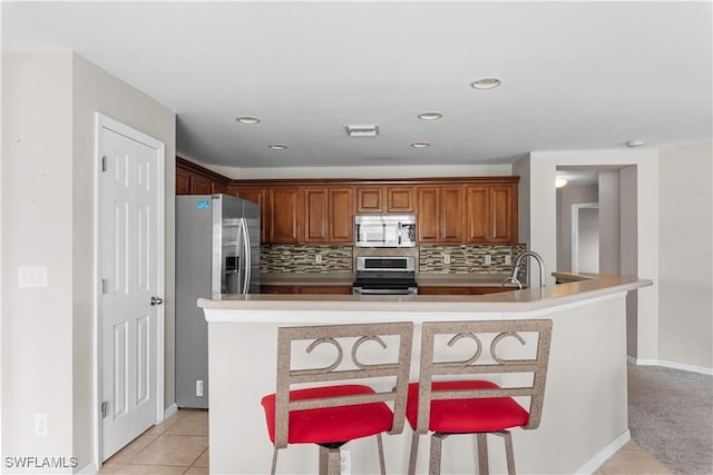 kitchen featuring sink, a breakfast bar area, stainless steel appliances, light tile patterned flooring, and decorative backsplash