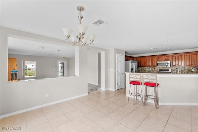 kitchen with light tile patterned flooring, appliances with stainless steel finishes, a kitchen breakfast bar, kitchen peninsula, and backsplash