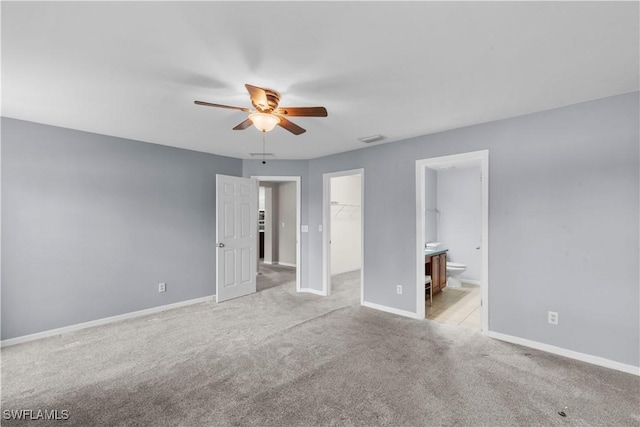 unfurnished bedroom with ensuite bathroom, a spacious closet, ceiling fan, light carpet, and a closet