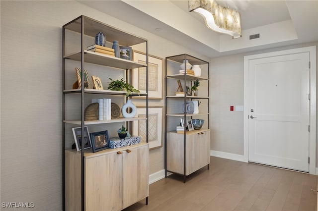 interior space featuring baseboards, visible vents, a raised ceiling, and wood finished floors