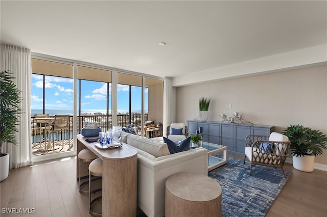 living area featuring expansive windows, a water view, wood finished floors, and baseboards