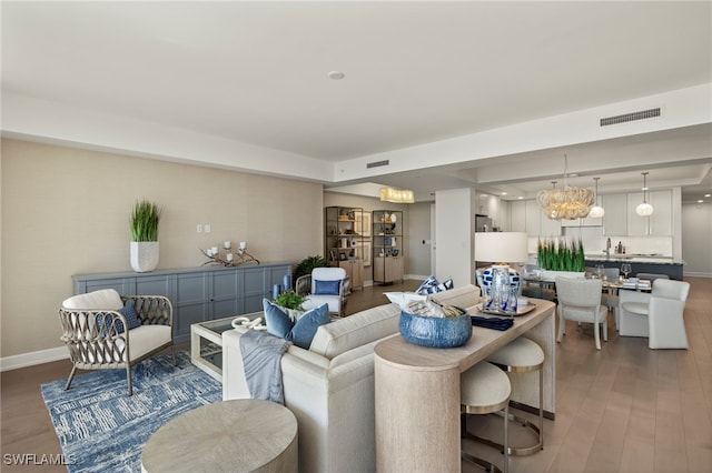 living room featuring a notable chandelier, wood finished floors, visible vents, and baseboards