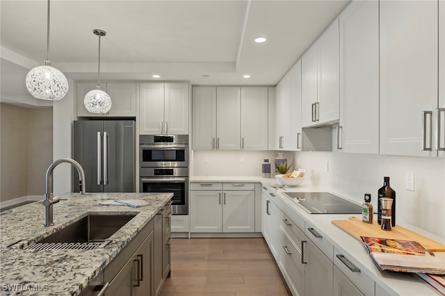 kitchen featuring light wood finished floors, appliances with stainless steel finishes, a tray ceiling, a sink, and recessed lighting