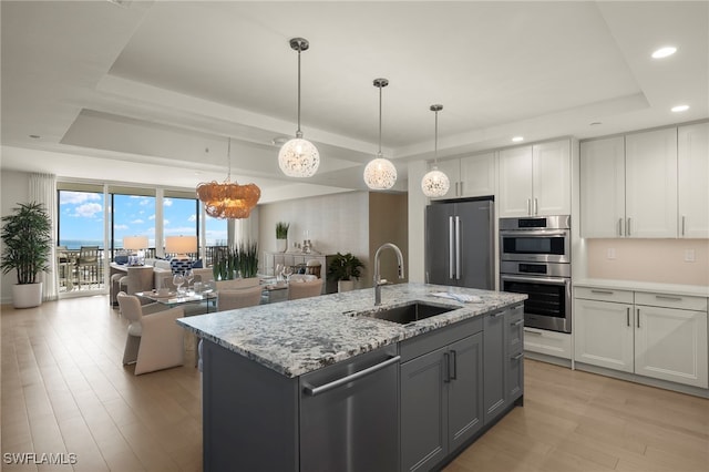 kitchen with stainless steel appliances, a raised ceiling, light wood-style flooring, white cabinets, and a sink