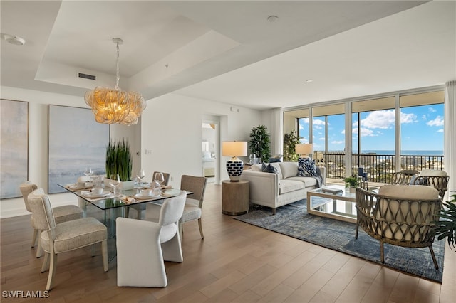 dining area featuring visible vents, a raised ceiling, wood finished floors, an inviting chandelier, and a wall of windows