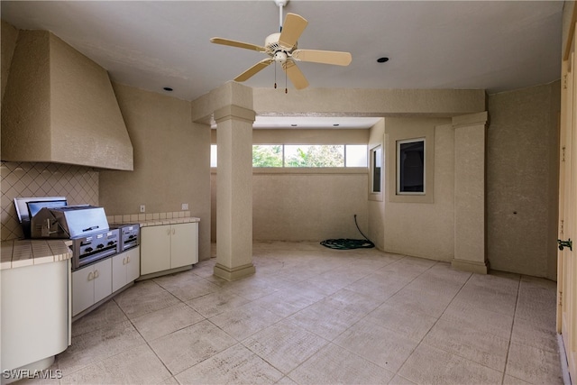 interior space with ceiling fan, decorative columns, tile counters, decorative backsplash, and white cabinets