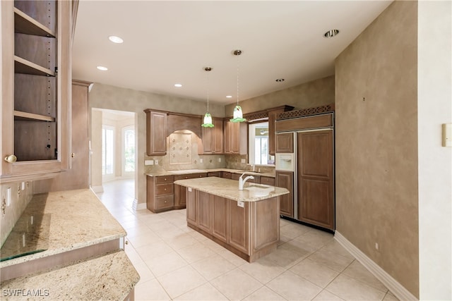 kitchen featuring hanging light fixtures, light stone countertops, a wealth of natural light, and paneled built in refrigerator