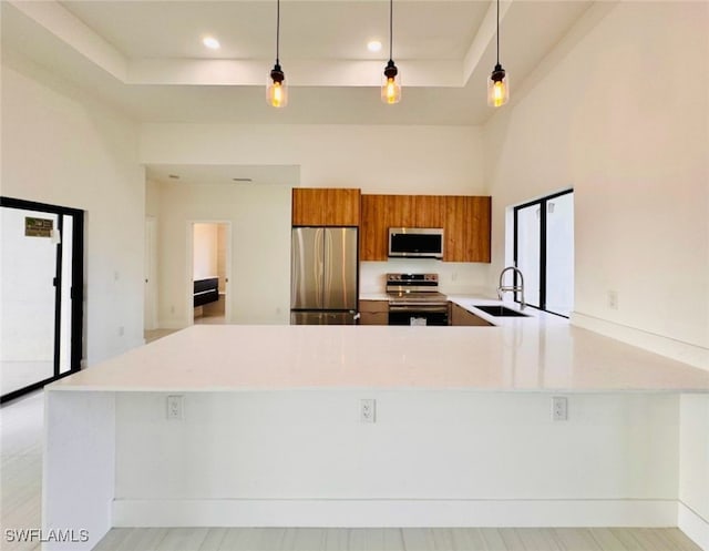 kitchen with a peninsula, a sink, light countertops, appliances with stainless steel finishes, and brown cabinets