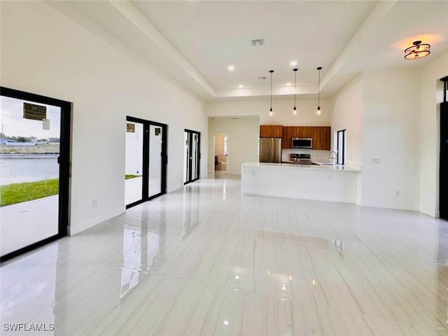 unfurnished living room featuring a high ceiling, a sink, visible vents, baseboards, and a raised ceiling