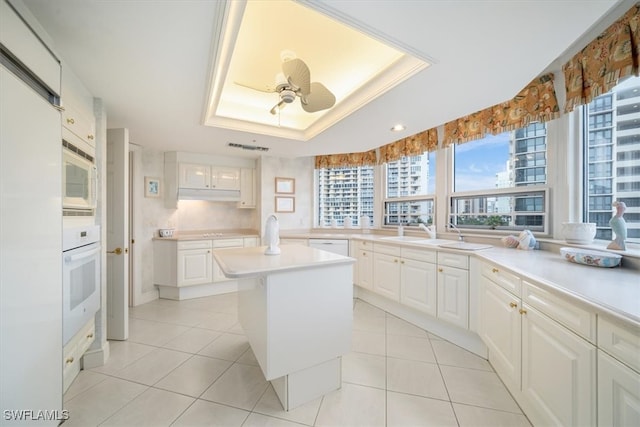 kitchen featuring a kitchen island, white cabinetry, white appliances, and a raised ceiling