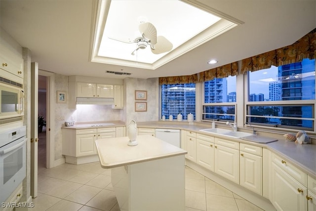 kitchen with a tray ceiling, sink, a center island, white appliances, and ceiling fan