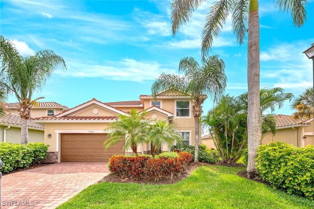 mediterranean / spanish house featuring a garage, a tiled roof, decorative driveway, stucco siding, and a front yard