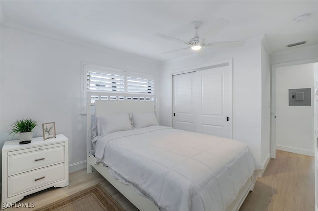 bedroom featuring electric panel, ceiling fan, light hardwood / wood-style floors, crown molding, and a closet