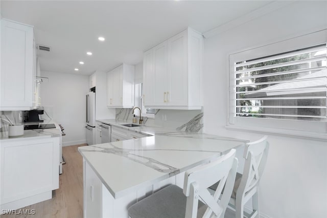 kitchen with fridge, kitchen peninsula, sink, and white cabinets