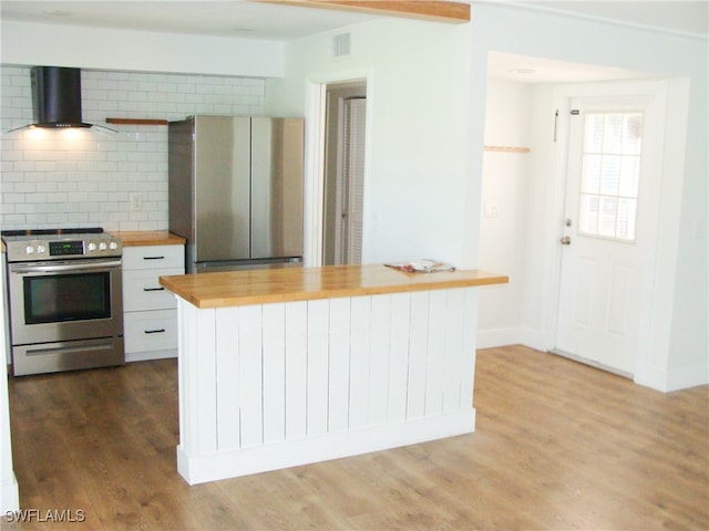 kitchen with appliances with stainless steel finishes, dark wood-type flooring, tasteful backsplash, wood counters, and wall chimney range hood