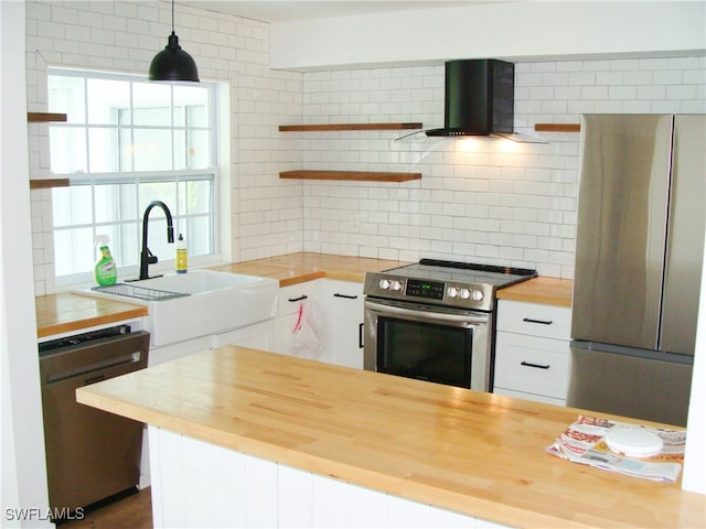 kitchen featuring decorative light fixtures, appliances with stainless steel finishes, wall chimney exhaust hood, and wood counters