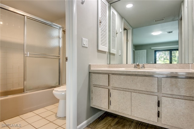 full bathroom featuring tile patterned flooring, bath / shower combo with glass door, vanity, and toilet