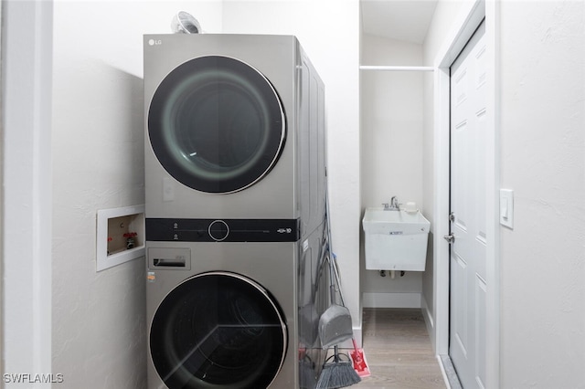 washroom featuring sink, wood-type flooring, and stacked washer and clothes dryer