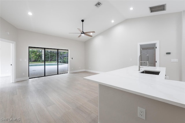 unfurnished living room with ceiling fan, sink, high vaulted ceiling, and light wood-type flooring