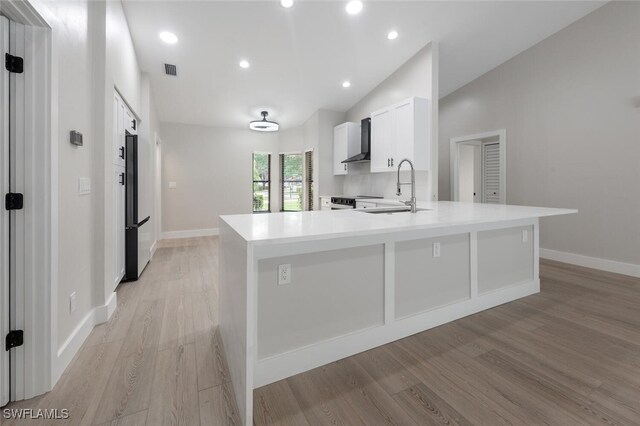 kitchen with sink, wall chimney exhaust hood, light hardwood / wood-style flooring, lofted ceiling, and white cabinets