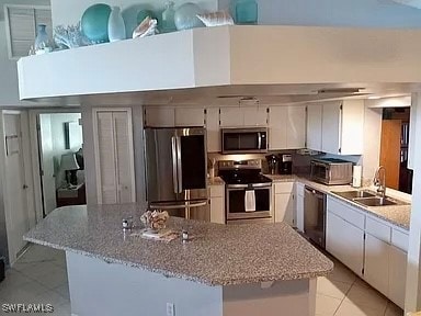 kitchen with white cabinetry, light stone counters, light tile patterned floors, stainless steel appliances, and sink