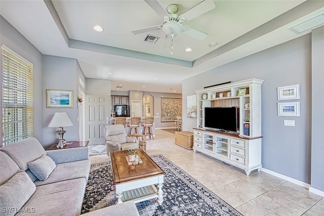 living room with ceiling fan, light tile patterned flooring, and a tray ceiling