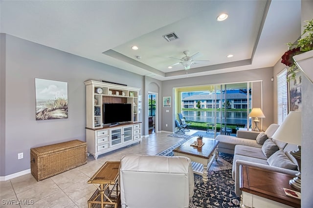 living room with ceiling fan, a tray ceiling, and light tile patterned floors