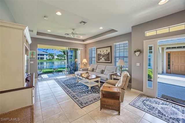 tiled living room with a tray ceiling and ceiling fan