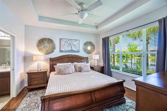 bedroom with a tray ceiling, ceiling fan, ensuite bathroom, and hardwood / wood-style floors