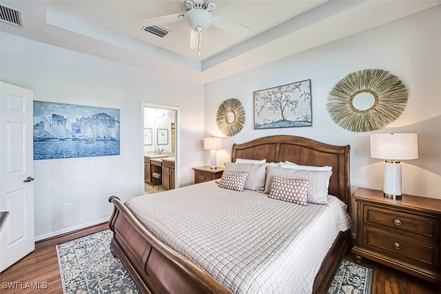 bedroom with ceiling fan, sink, a tray ceiling, ensuite bathroom, and dark hardwood / wood-style flooring