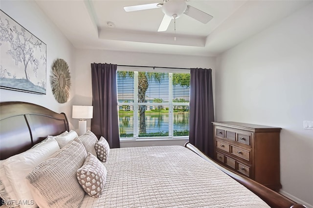 bedroom with a raised ceiling, a water view, and ceiling fan